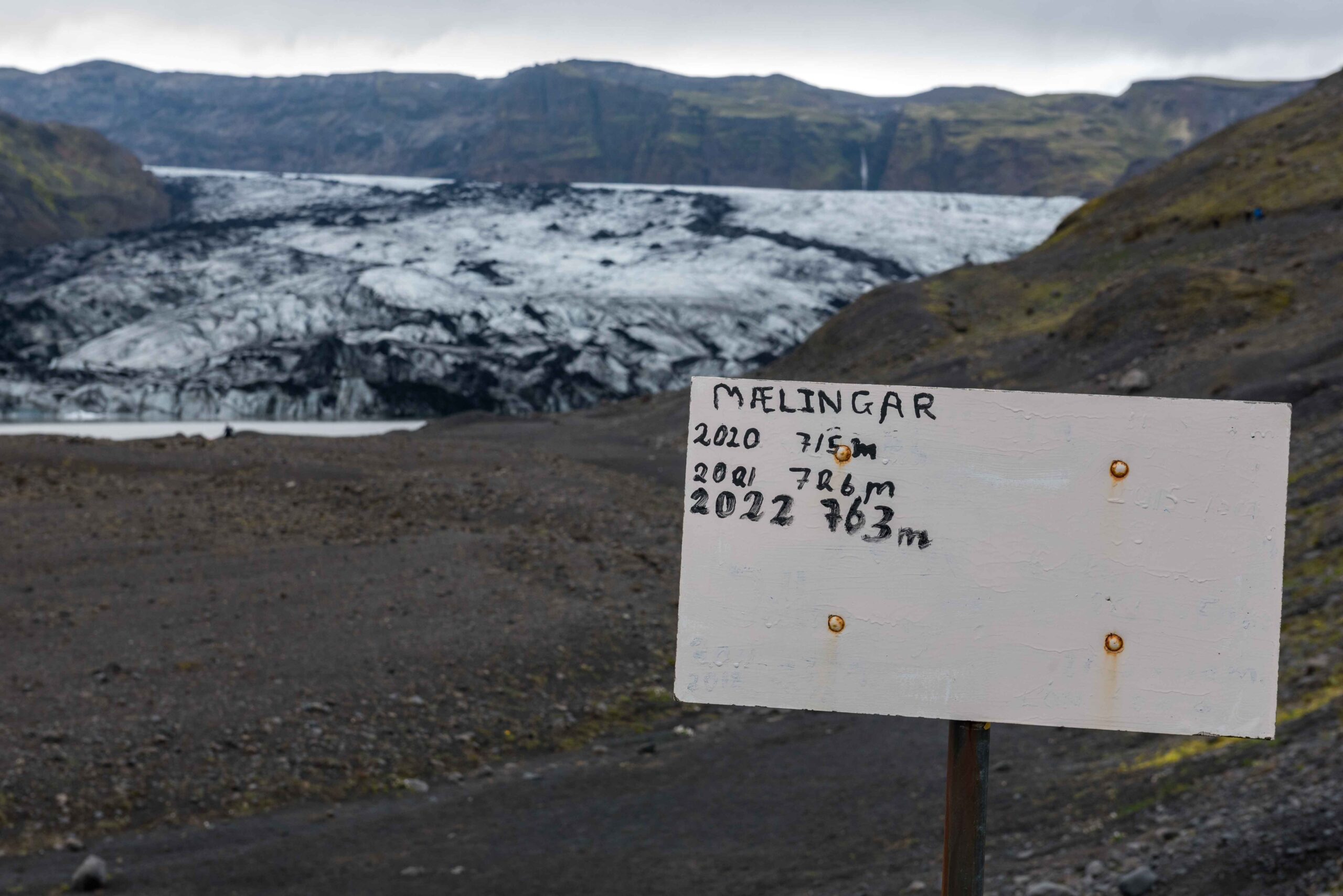 Kinderen van een IJslandse school meten sinds 2010 jaarlijks de verandering en schrijven hun metingen (mælingar) op een bordje. In twaalf jaar zijn is de gletsjer 763 meter korter geworden.