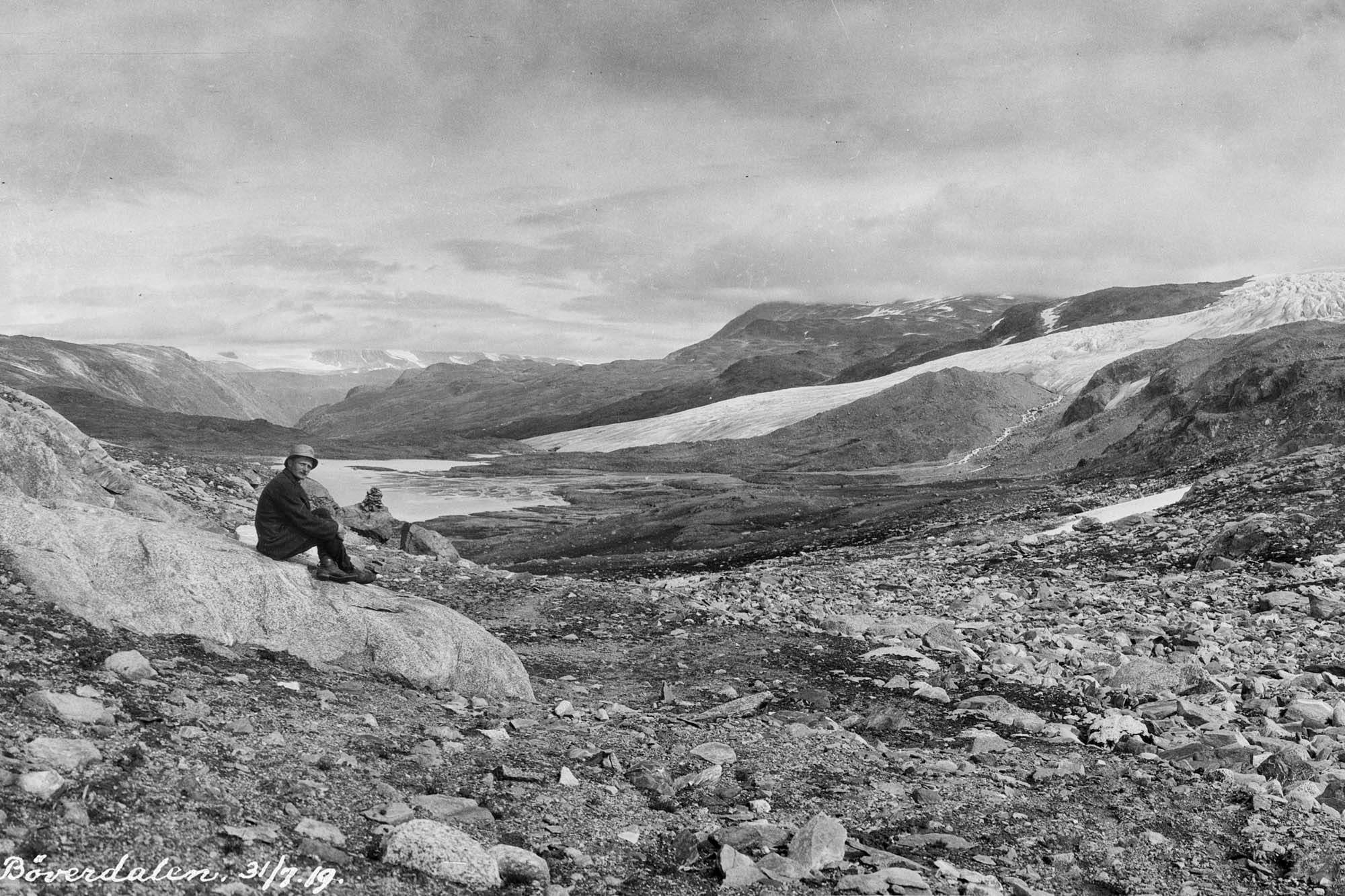 De Bøverbreen in 1919, toen de tong nog tot in het dal reikte. Het meer achter de man is een overblijfsel van het door de gletsjer afgedamde Bøvervatnet. Fotograaf: Jørgen Grundtvig-Olsen, Bibliotheek Universiteit van Bergen ubb-go-a-0686.