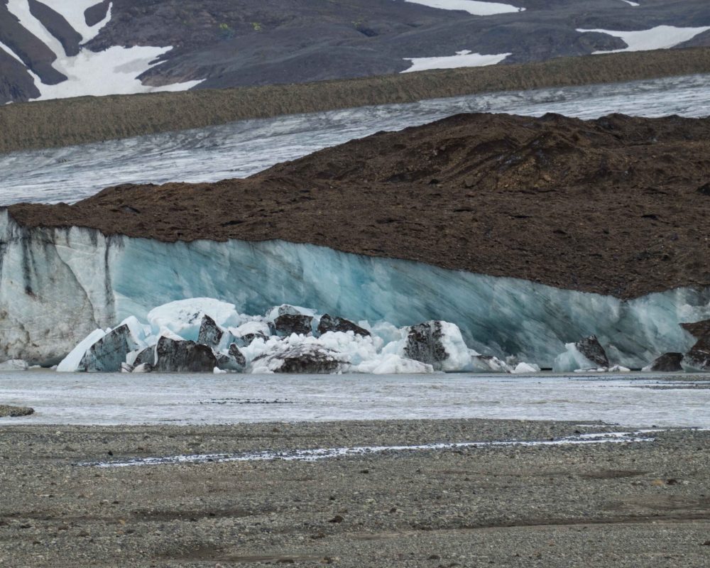 Een dunne laag stenen van de westelijke middenmorene isoleert het ijs, juni 2023.